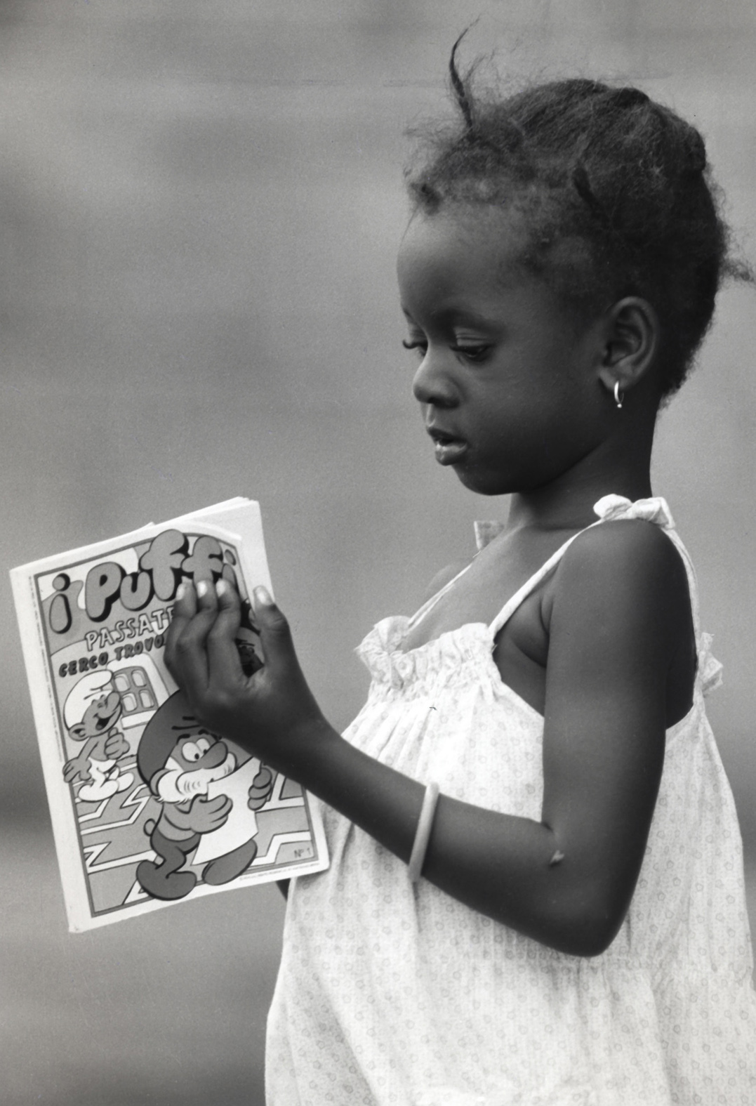 Castel Volturno, 1988 - Bambina africana con un fumetto dei puffi ed una mosca sul braccio